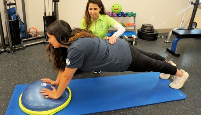 woman in plank position on a balance ball with help from a physiotherapist